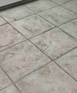 Close-up of kitchen floor tiles showing several shoe and partial footprints in light dust or dirt.