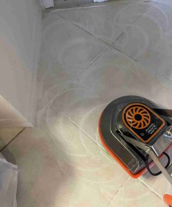 A floor cleaning machine is being used on tiled flooring, leaving circular cleaning marks on the surface.