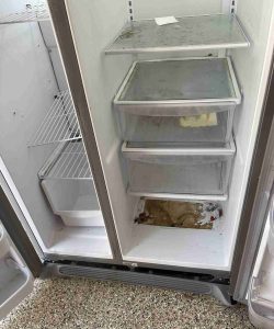 Open refrigerator with dirty shelves and drawers, some food residue inside, and visible dirt on the bottom interior.