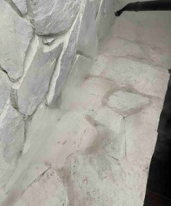 A vacuum hose is cleaning dust from a light-colored stone surface next to a stone wall.