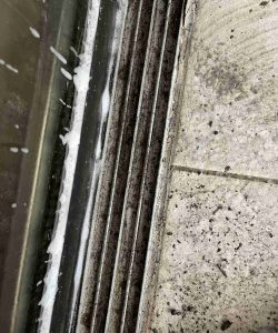 Close-up of a dirty floor drain with grime and debris on the surrounding tile and metal grate.