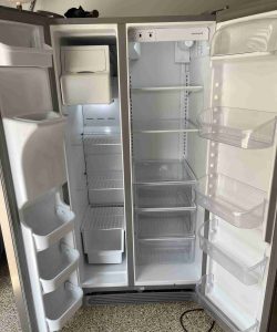 An open, empty side-by-side refrigerator and freezer with shelves and door compartments visible.