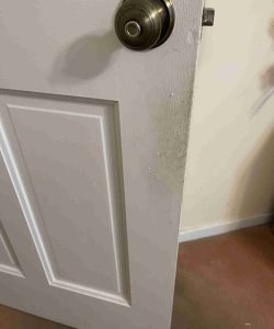 A white door with a brass knob is partially open, showing a scuffed and discolored area near the edge.