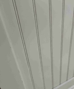 Close-up of a light-colored paneled surface with vertical grooves and a horizontal trim at the bottom.