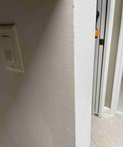 A close-up of a white wall corner next to a light switch and an open doorway in a tiled room.