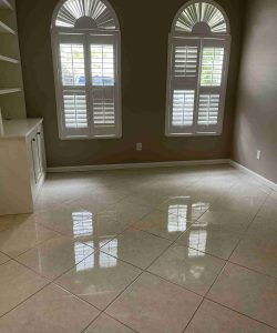 Empty room with shiny tiled floor, two arched windows with shutters, and built-in shelving on the left wall.