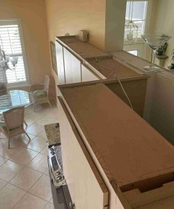 View from above kitchen cabinets showing dust and wires, overlooking a dining area with a glass table and chairs.