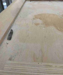 A dusty wooden surface with debris and a small rectangular dark object near the edge.