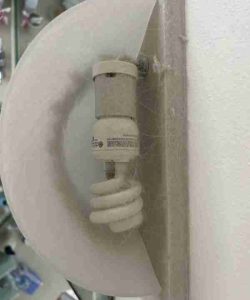 Dusty and cobweb-covered spiral light bulb fixture mounted on a wall near a mirror.