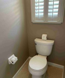 A toilet with a roll of toilet paper on top of the tank and another roll on the wall-mounted holder beside it.