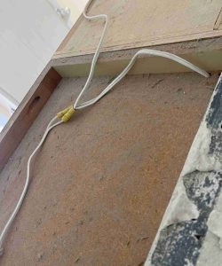 A white electrical wire with a yellow connector is lying on a dusty wooden surface near a partially painted area.