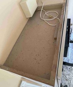 A dusty countertop with a white power cord and a wall-mounted box, with some scattered debris visible.