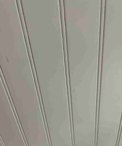 Close-up view of a white paneled surface with vertical and diagonal grooves, possibly part of a wall or ceiling.