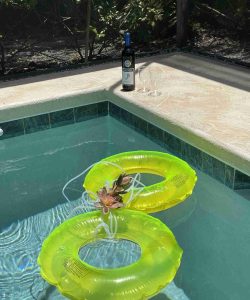 Two yellow pool floats in a swimming pool with a bottle of wine and two glasses on the poolside.