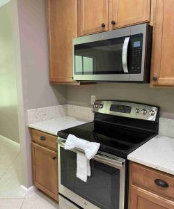 Modern kitchen with stainless steel microwave and electric stove, wooden cabinets, and a white towel on the oven handle.