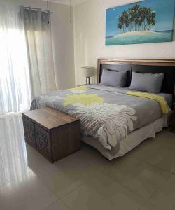 A tidy bedroom with a double bed, floral bedding, a wooden chest, and a beach painting above the headboard.